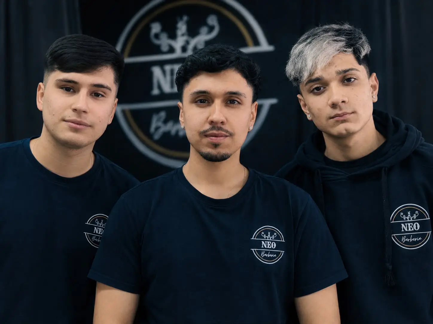 Los tres integrantes del equipo de Neo Barbería frente al logo del local